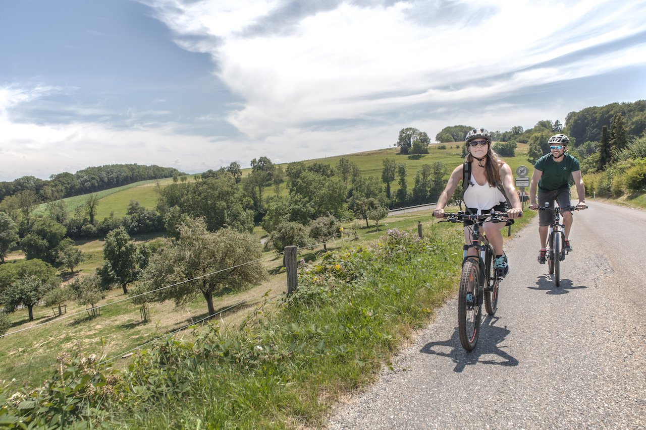 2 cyclistes sur une route, au pied du Jura