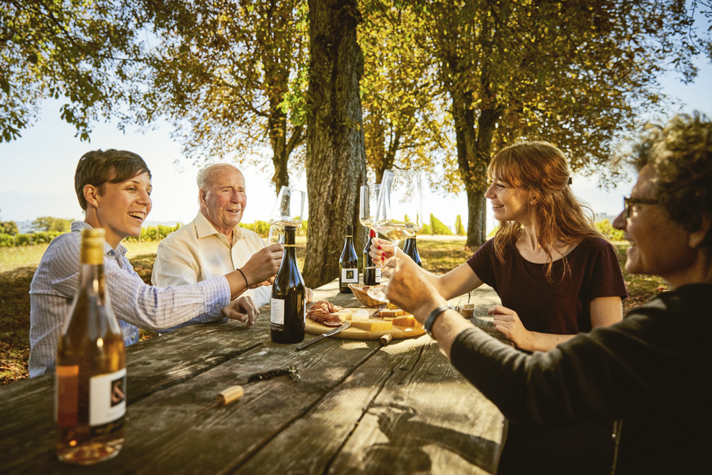 Groupe de quatre personnes partageant un apéritif autour d'une table au milieu des vignes.